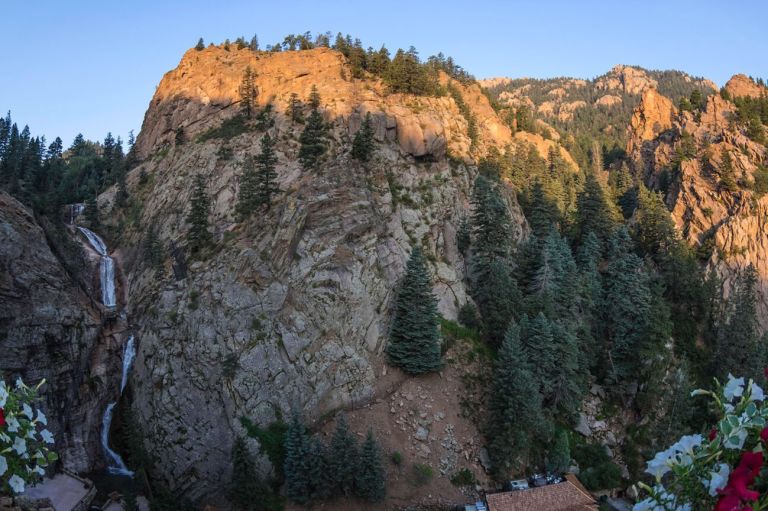 A Rocky Mountain With Trees And Flowers